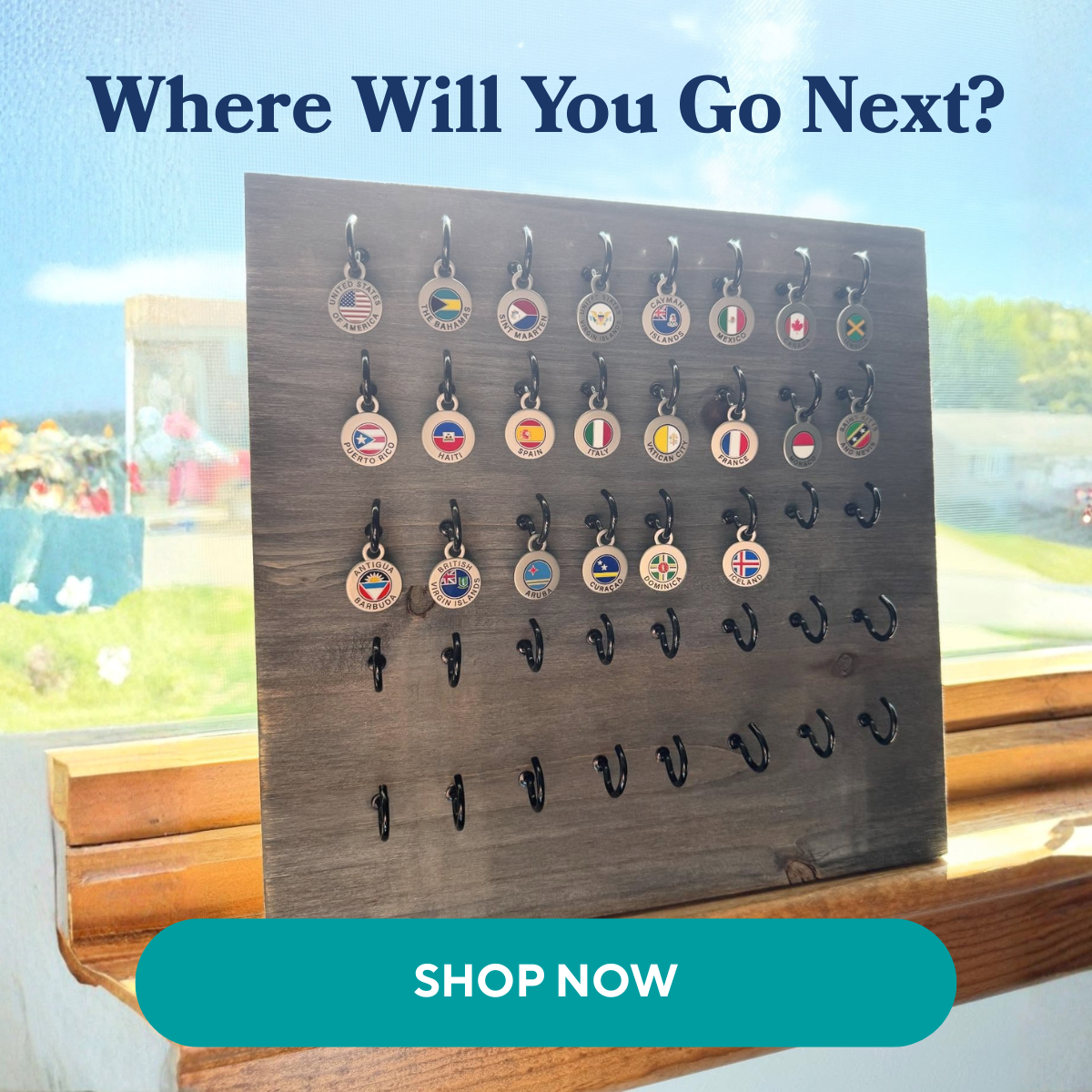A wooden display board holds various small, circular charms, each featuring a country's flag and name, displayed in a sunlit window. Overlay text asks "Where Wi