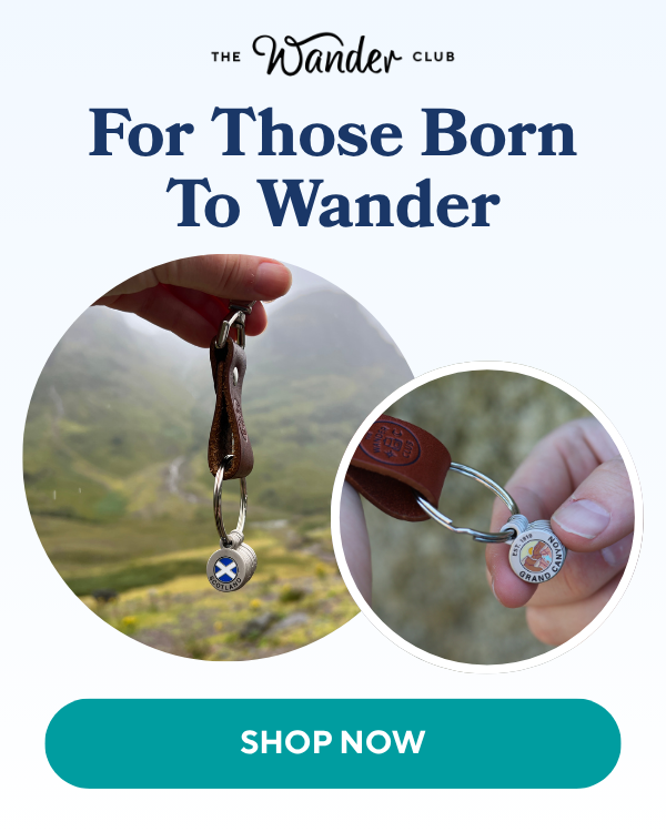 Hands holding two distinct leather keychains with travel-themed charms, one for Scotland and one for Grand Canyon, against blurred outdoor scenic backgrounds.