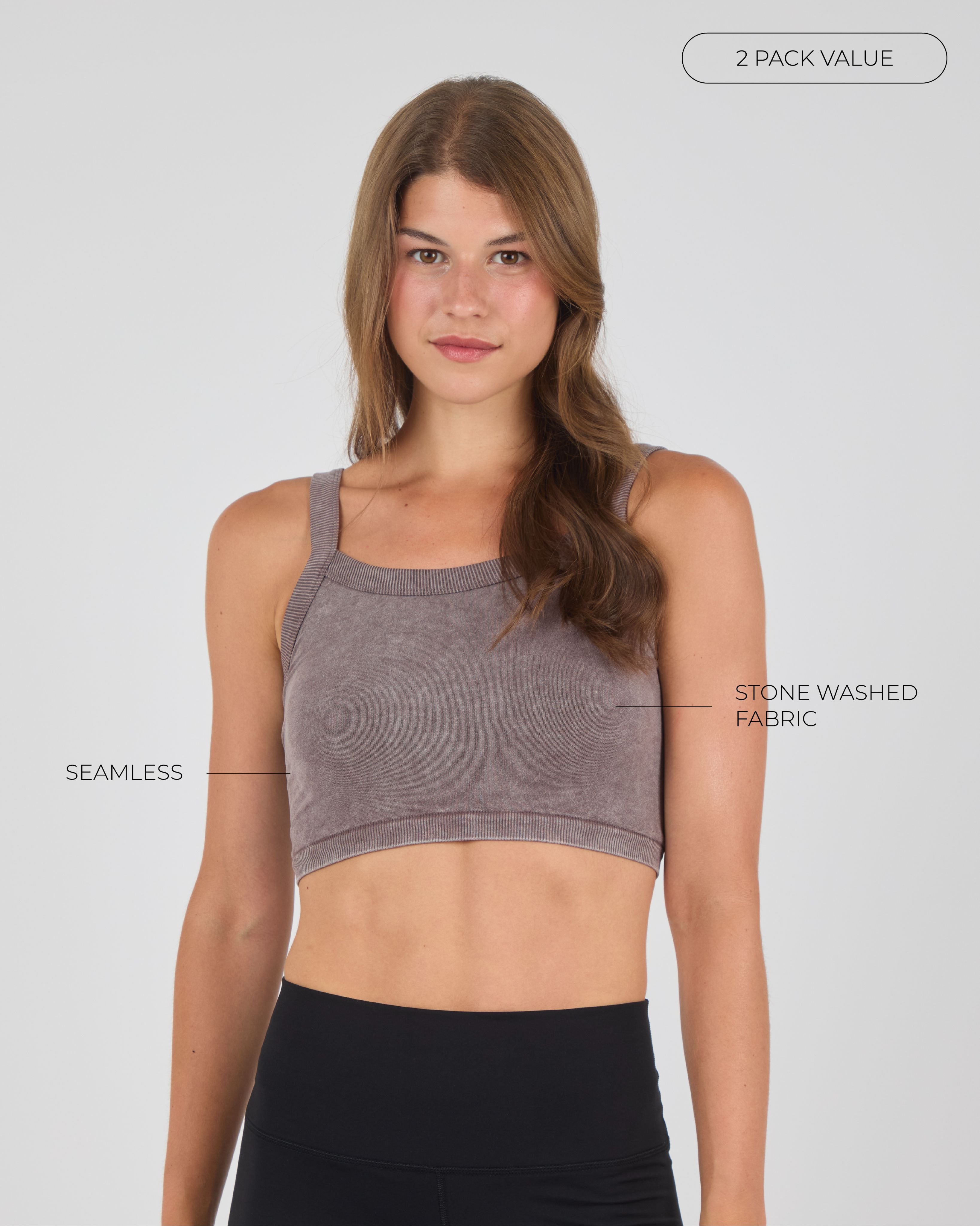 A young woman with brown hair faces the camera, wearing a brown stone-washed seamless crop top and black leggings against a light gray background.