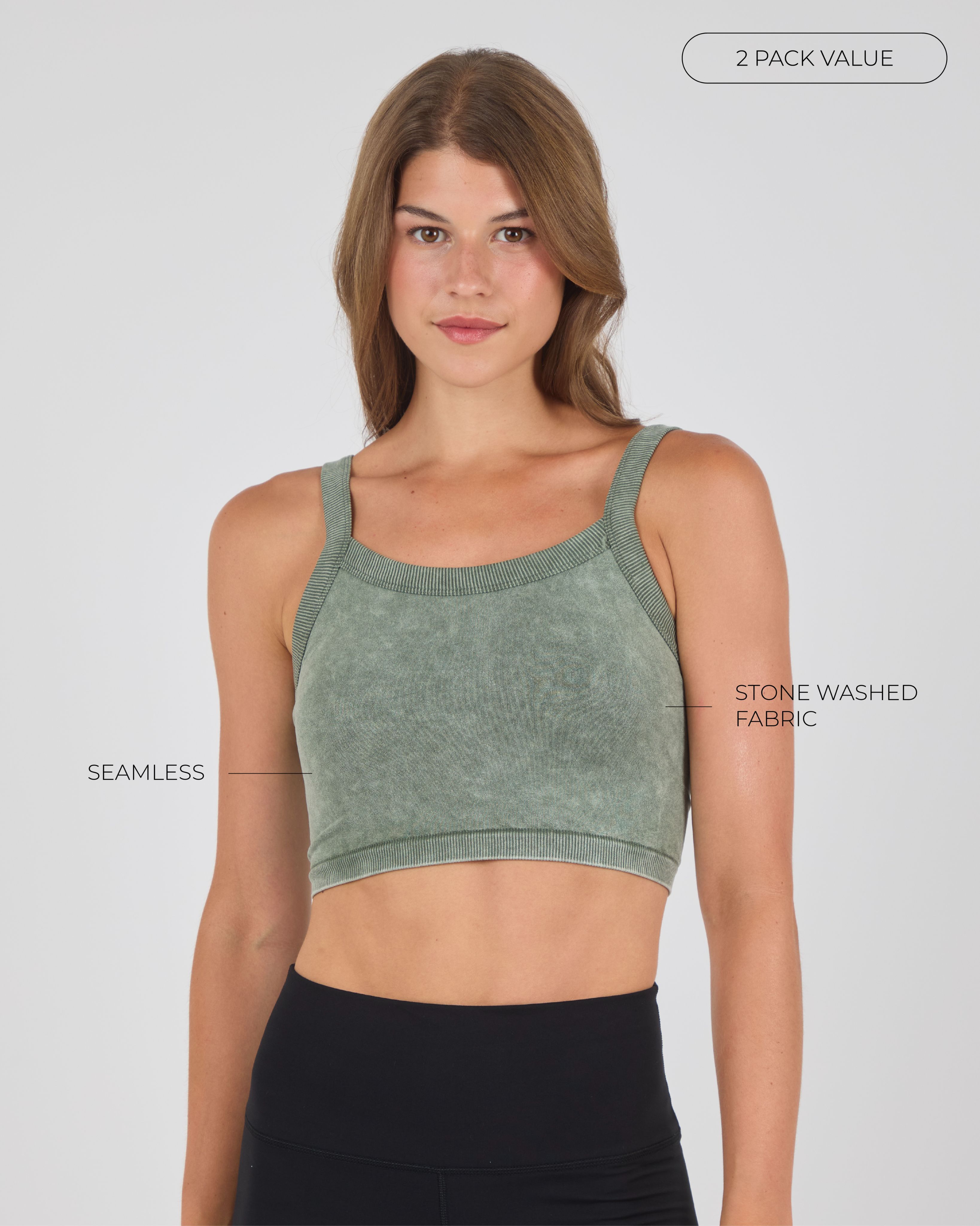 A woman with brown hair facing forward, wearing a sage green seamless sports top and black leggings against a light gray studio background.